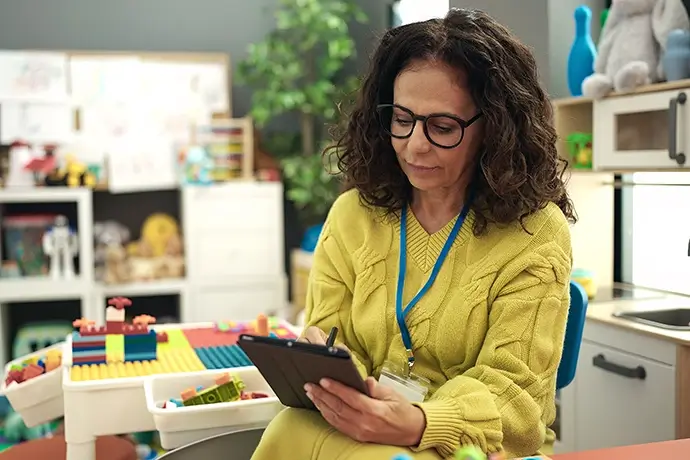 Middle age hispanic woman preschool teacher using touchpad at kindergarten