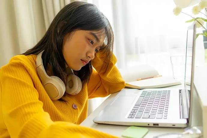 Frustrated Asian young girl student learning online class study in house. Teenage woman feel tired and stressed while using laptop computer device remote distancing study on table in bedroom at home.