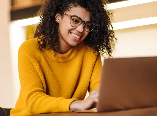 Image of cheerful African American woman in eyeglasses using laptop
